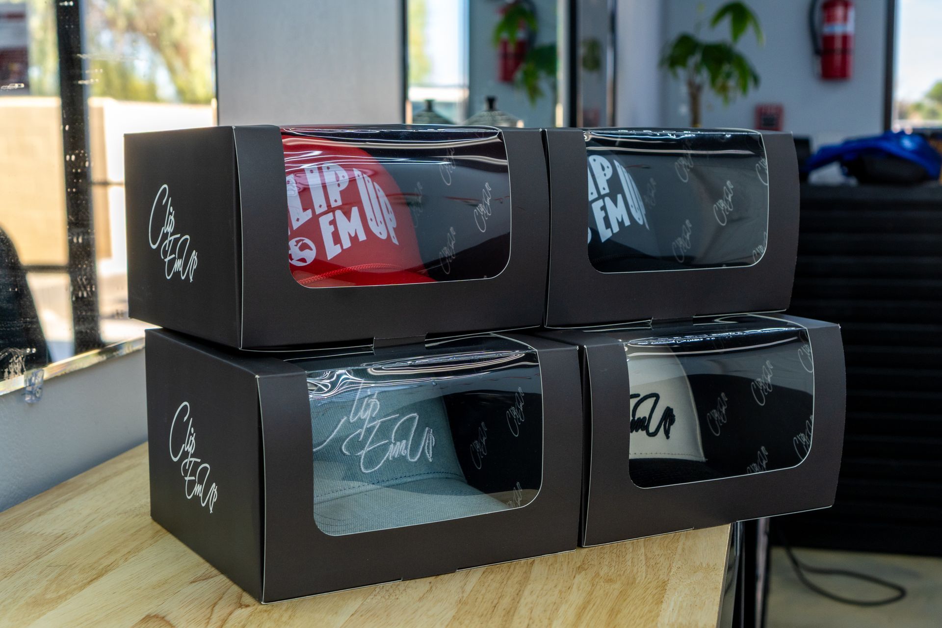 Four black cardboard display boxes stacked on a wooden table in a bright room