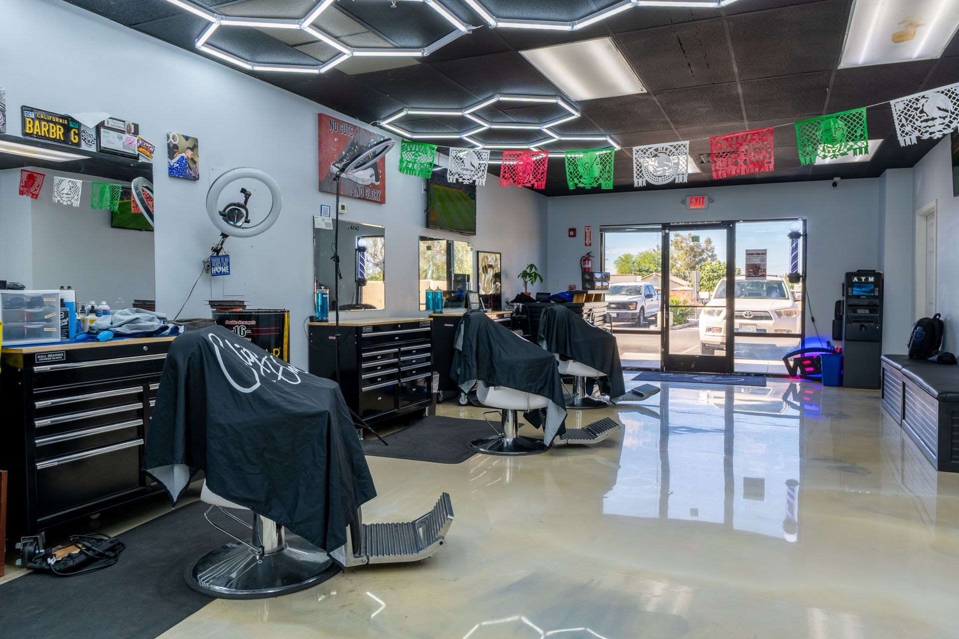 Modern barbershop interior with black chairs, mirrors, neon ceiling lights, and glossy floor.