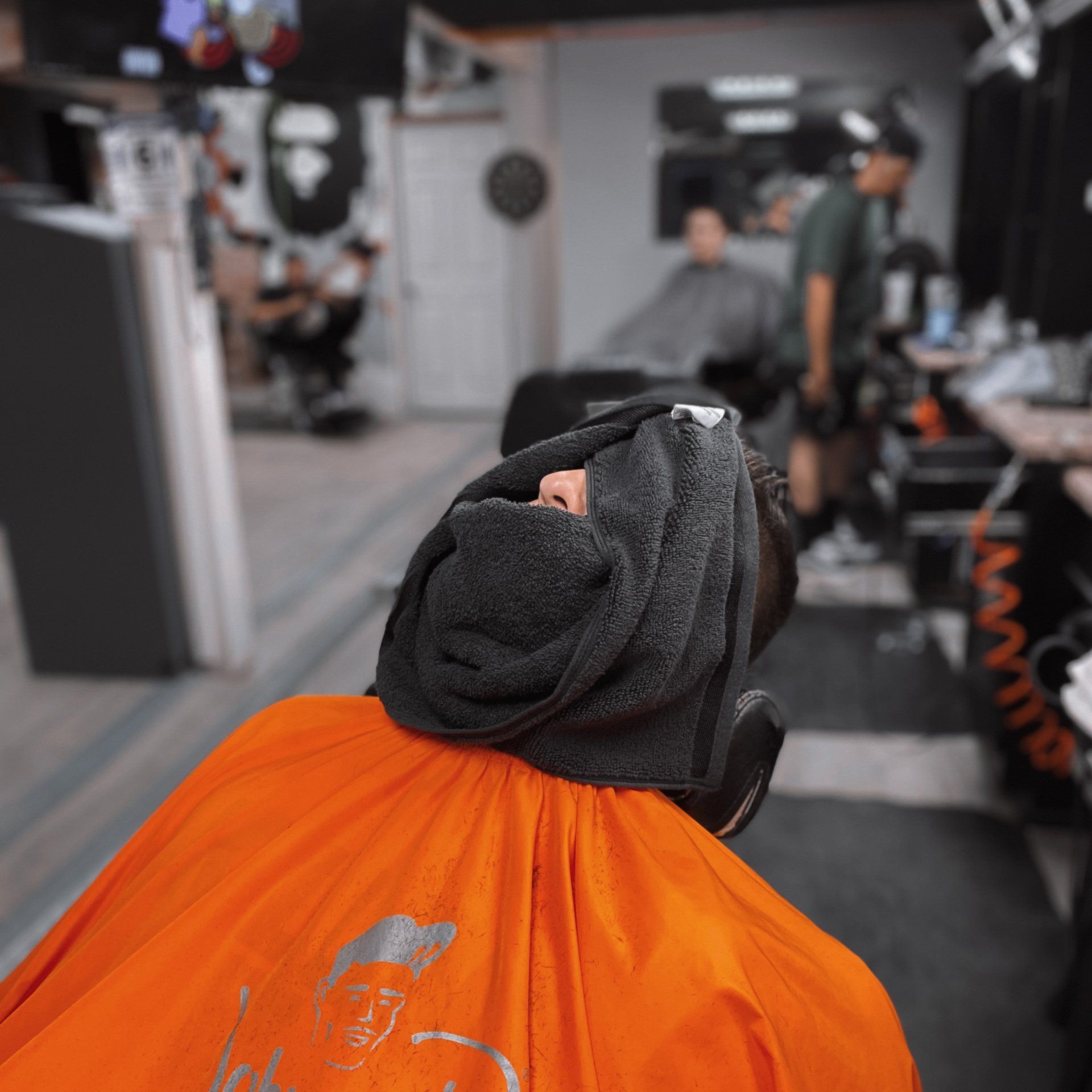 Black dog in an orange grooming cape at a pet salon with a towel over its head.