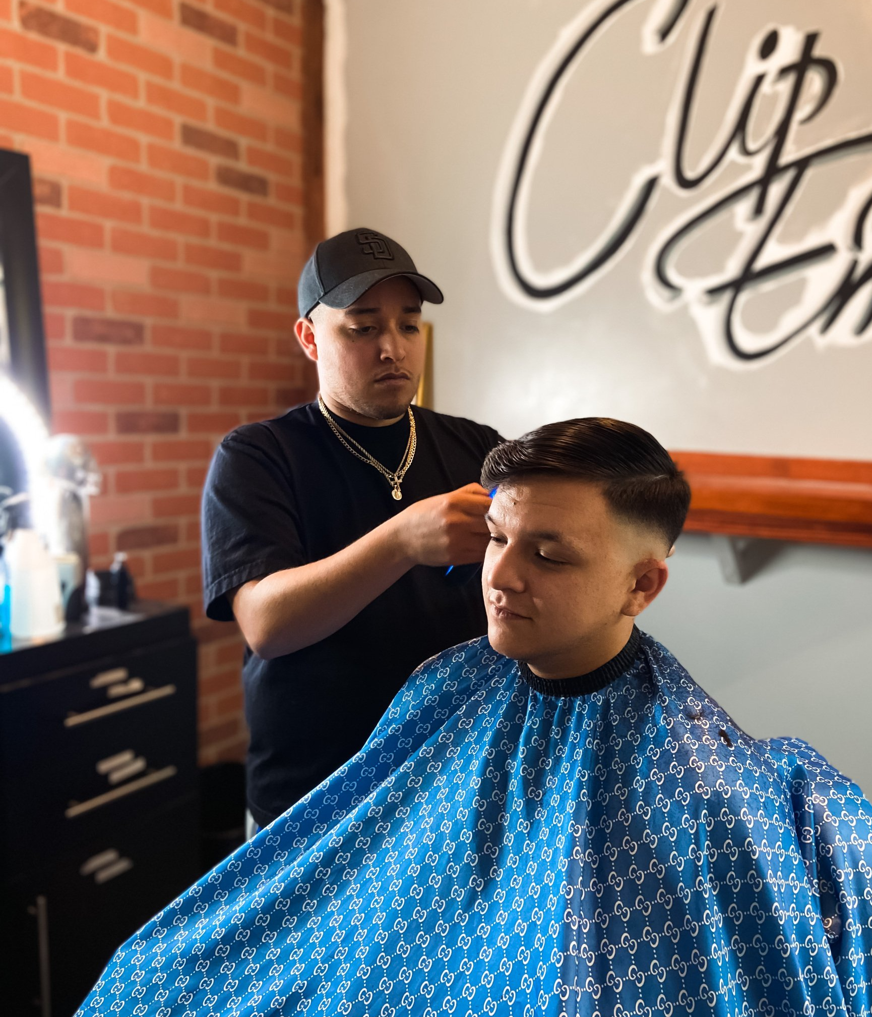 Barber trimming a client’s hair in a shop with brick walls and a blue cape