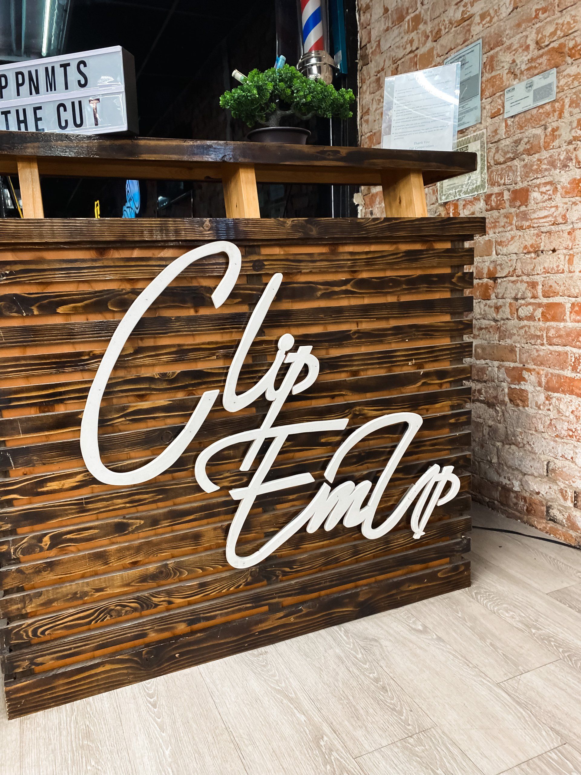Wooden bar counter with white “Clip & Chop” lettering in a brick-walled salon or café入口