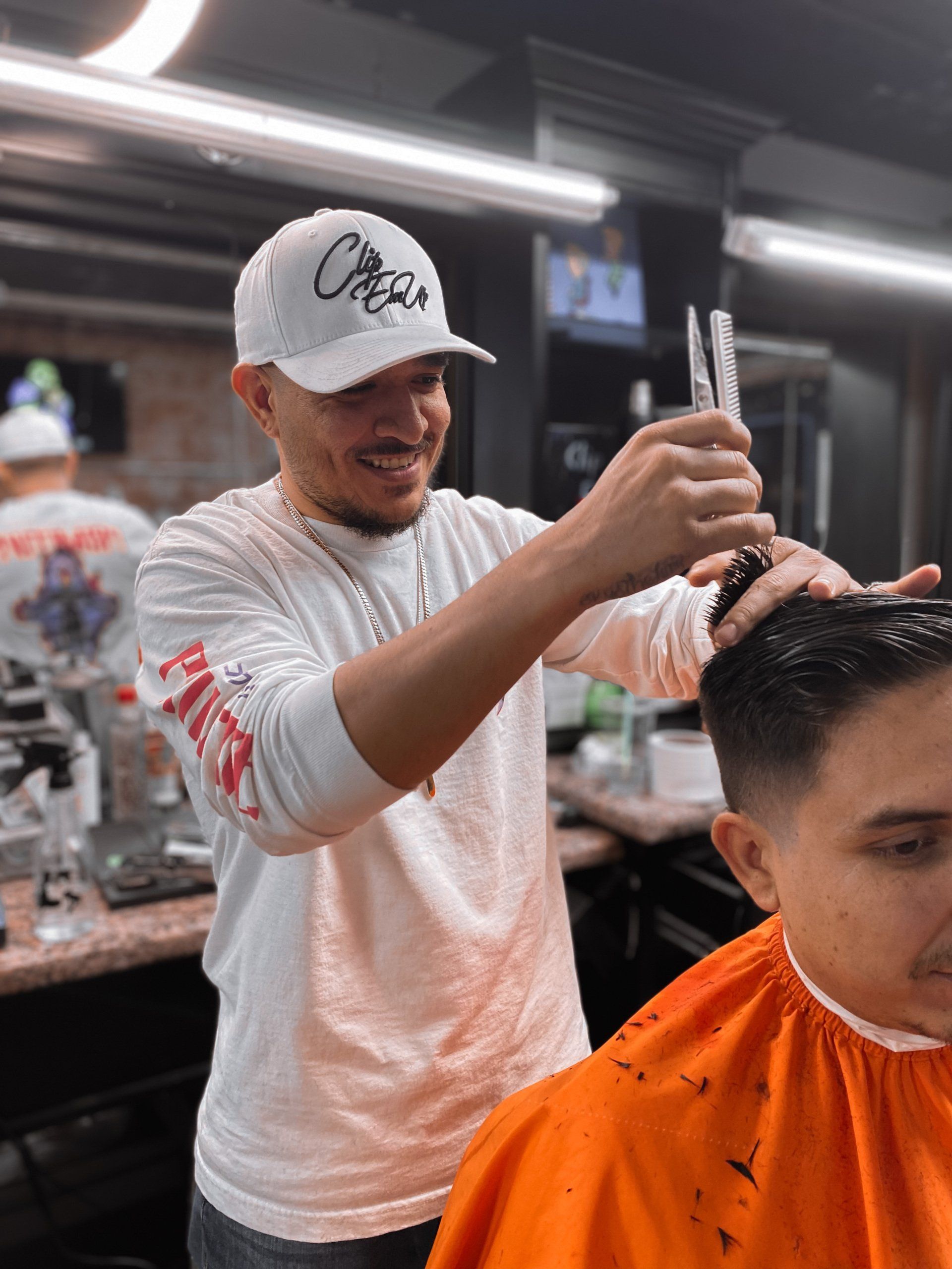 Barber cutting a client’s hair in a shop, with the client wearing an orange cape.