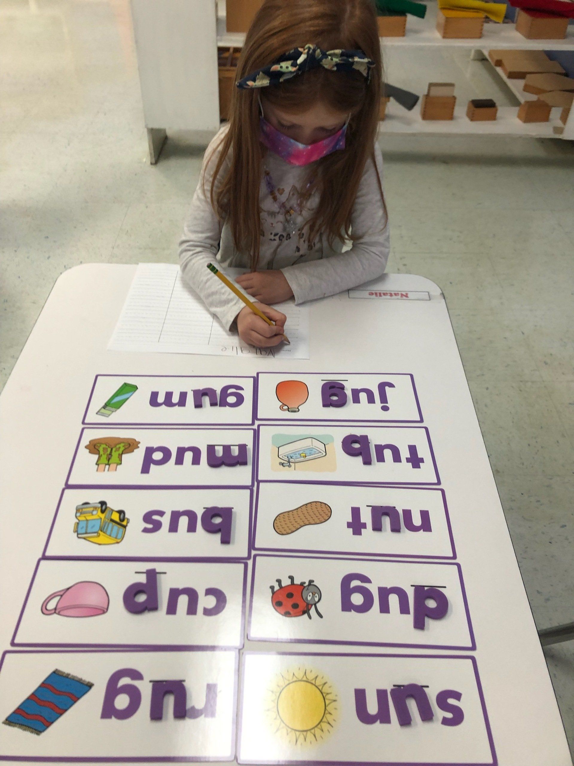 A little girl wearing a mask is writing on a piece of paper