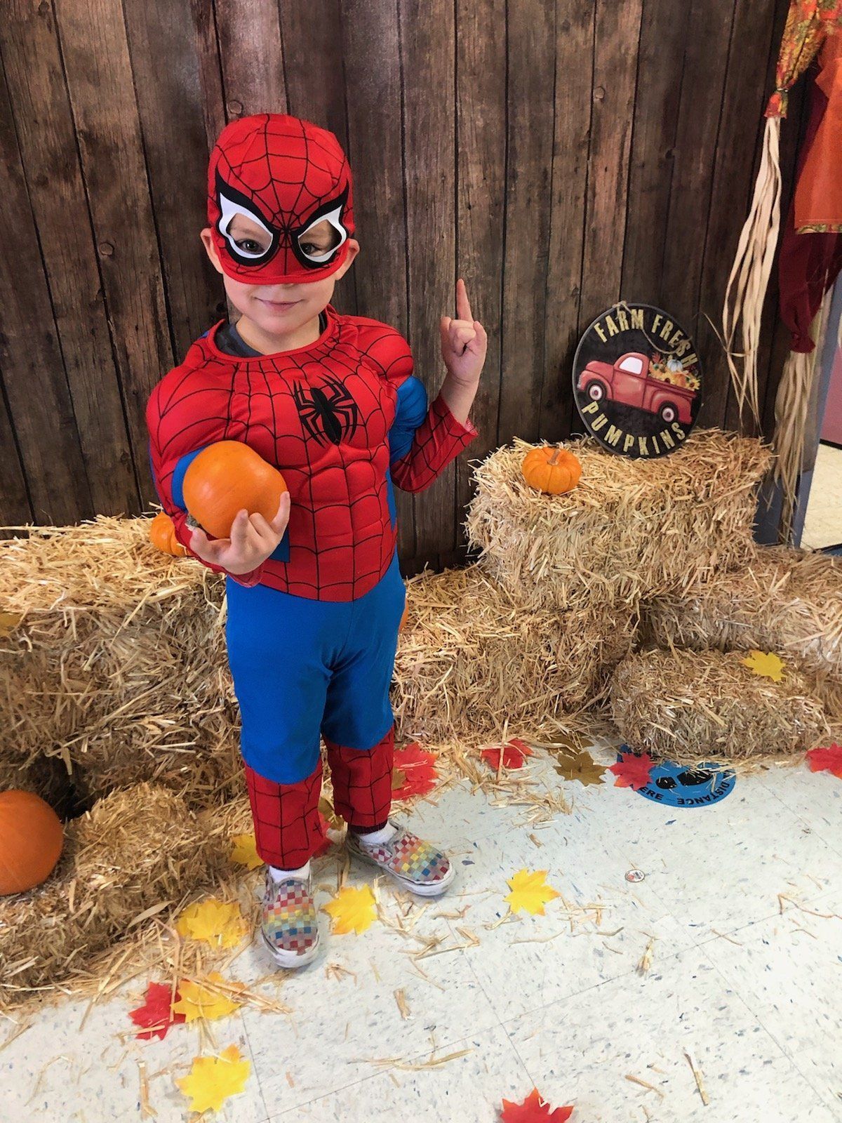 A young boy in a spiderman costume is holding a pumpkin.