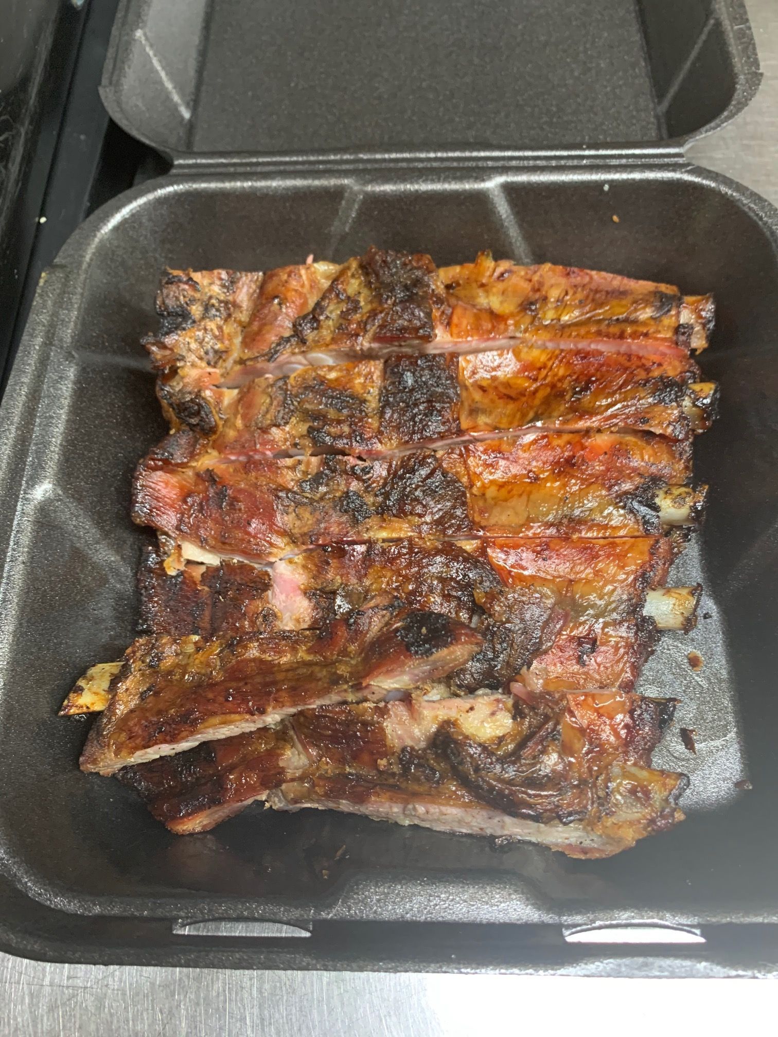 A styrofoam container filled with ribs is sitting on a table.