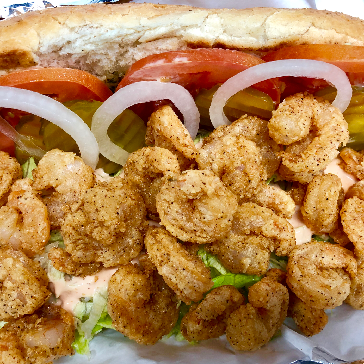 A fried shrimp sub sandwich with lettuce tomatoes and onions