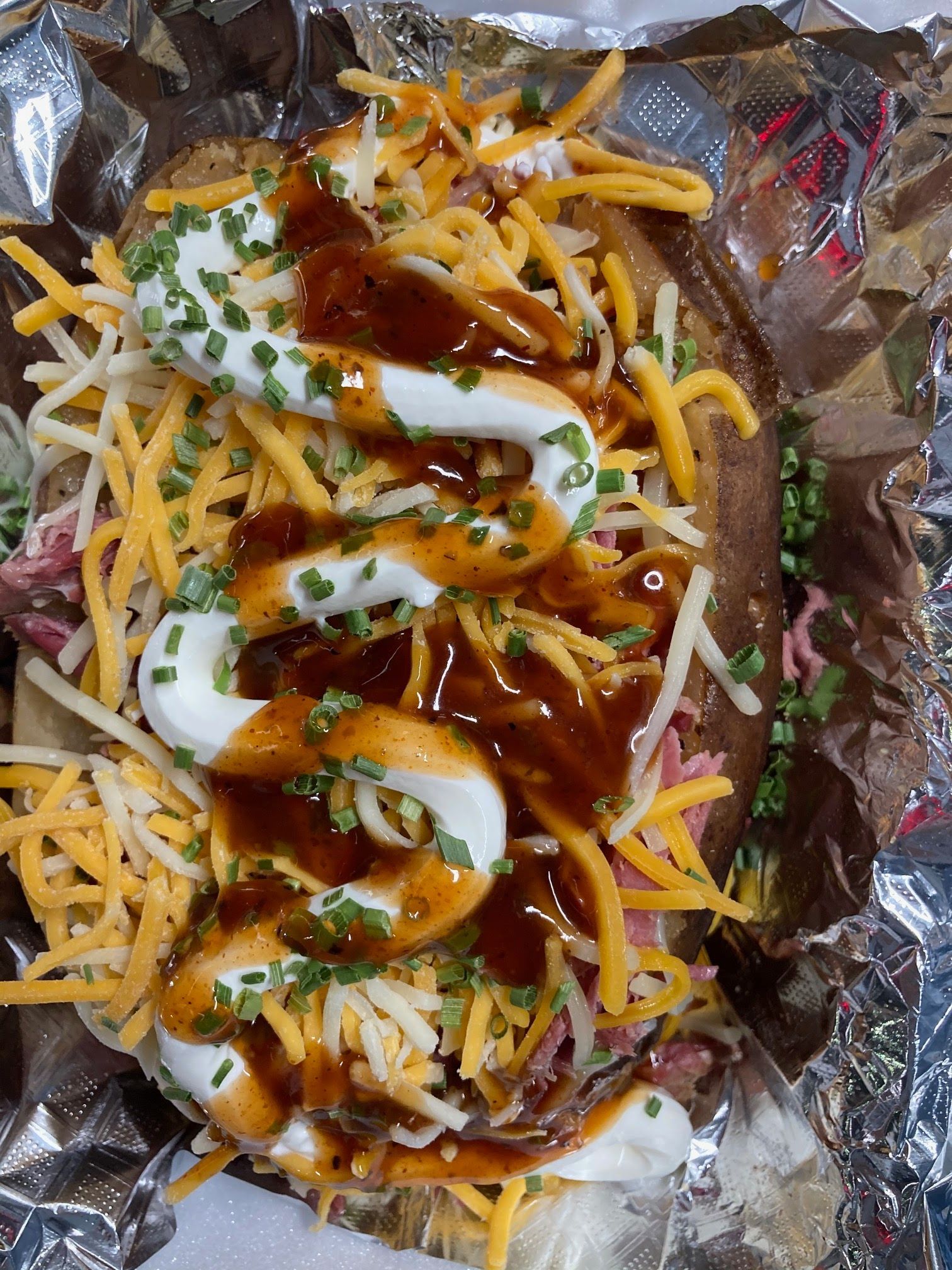 A baked potato covered in cheese , barbecue sauce and sour cream.