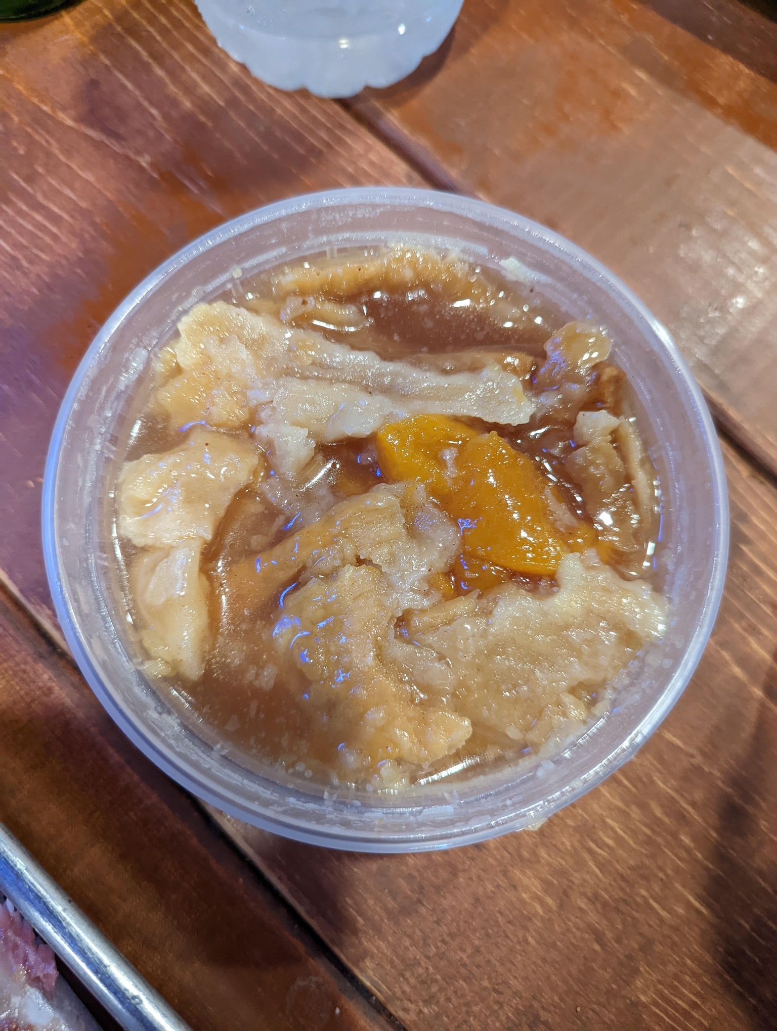 A bowl of peach cobbler is sitting on a wooden table.