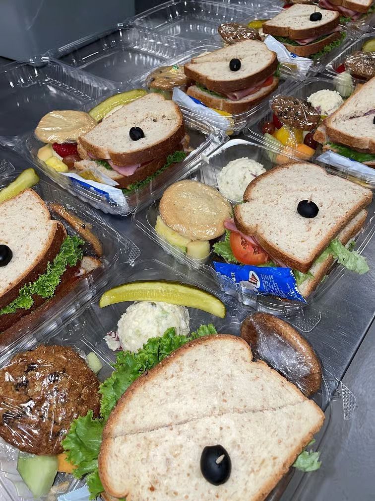 Prepared lunch trays with sandwiches, fruit, and snacks.