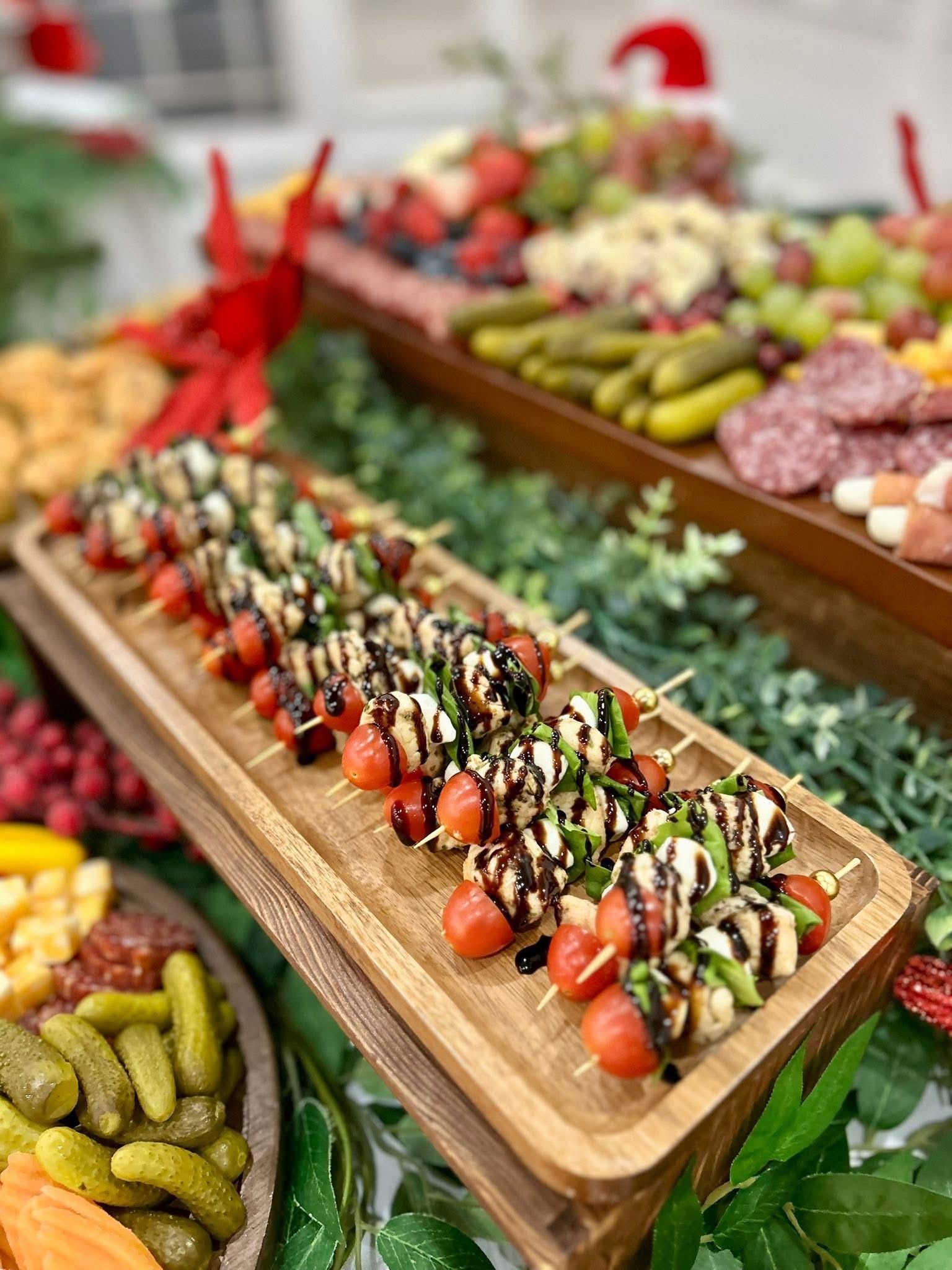 Wooden charcuterie boards with food including skewers, pickles, fruit, cheese, and salami.