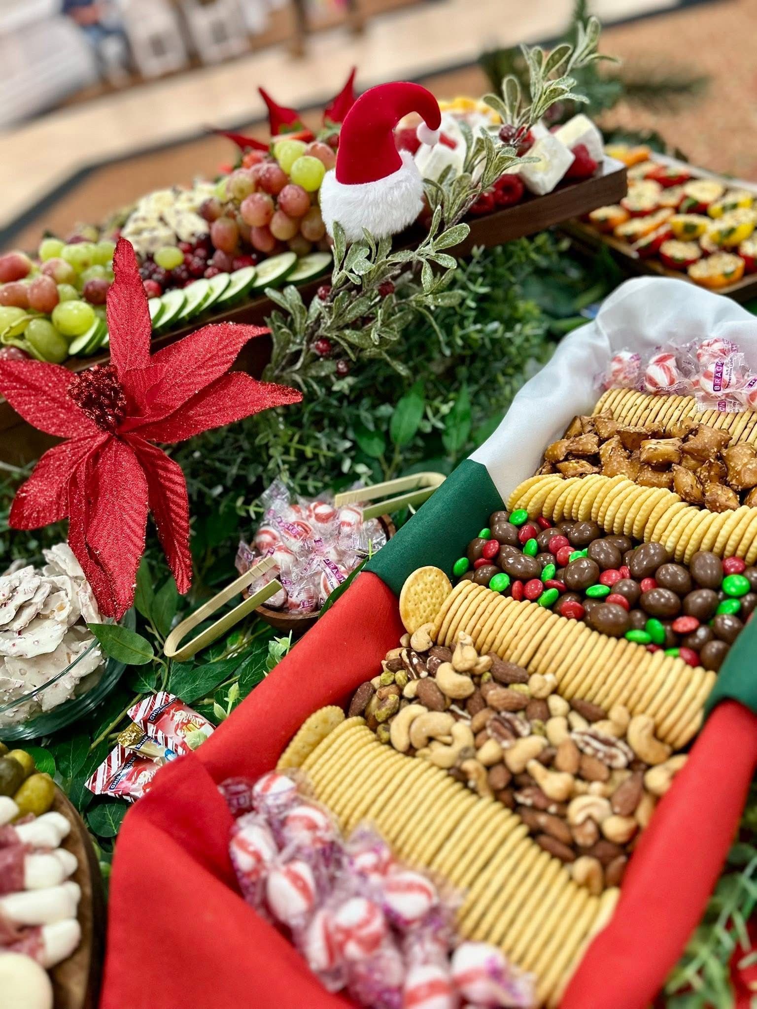 Holiday food display with cheeses, crackers, candies, nuts, and grapes, decorated with greenery and Santa hat.