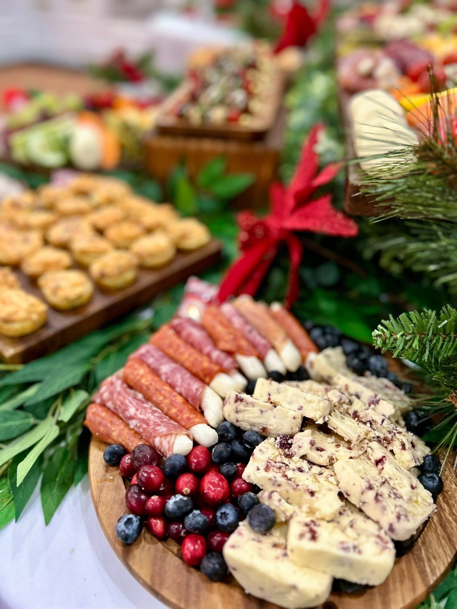 Charcuterie board overflowing with fruits, cheeses, meats, and vegetables, adorned with holiday greenery and red accents.