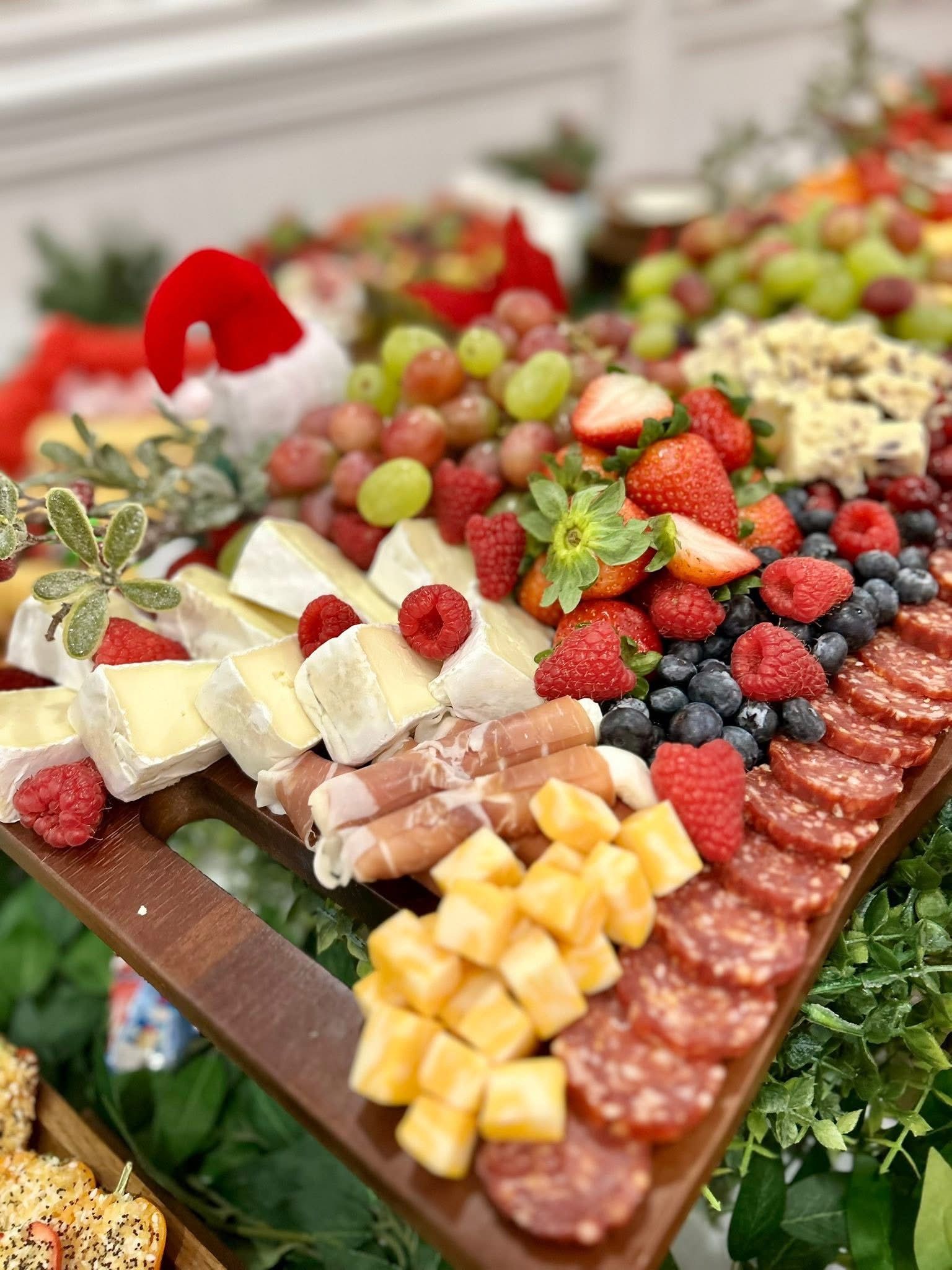 Christmas-themed charcuterie table with fruit, cheese, crackers, and holiday decorations, set on a white tablecloth.