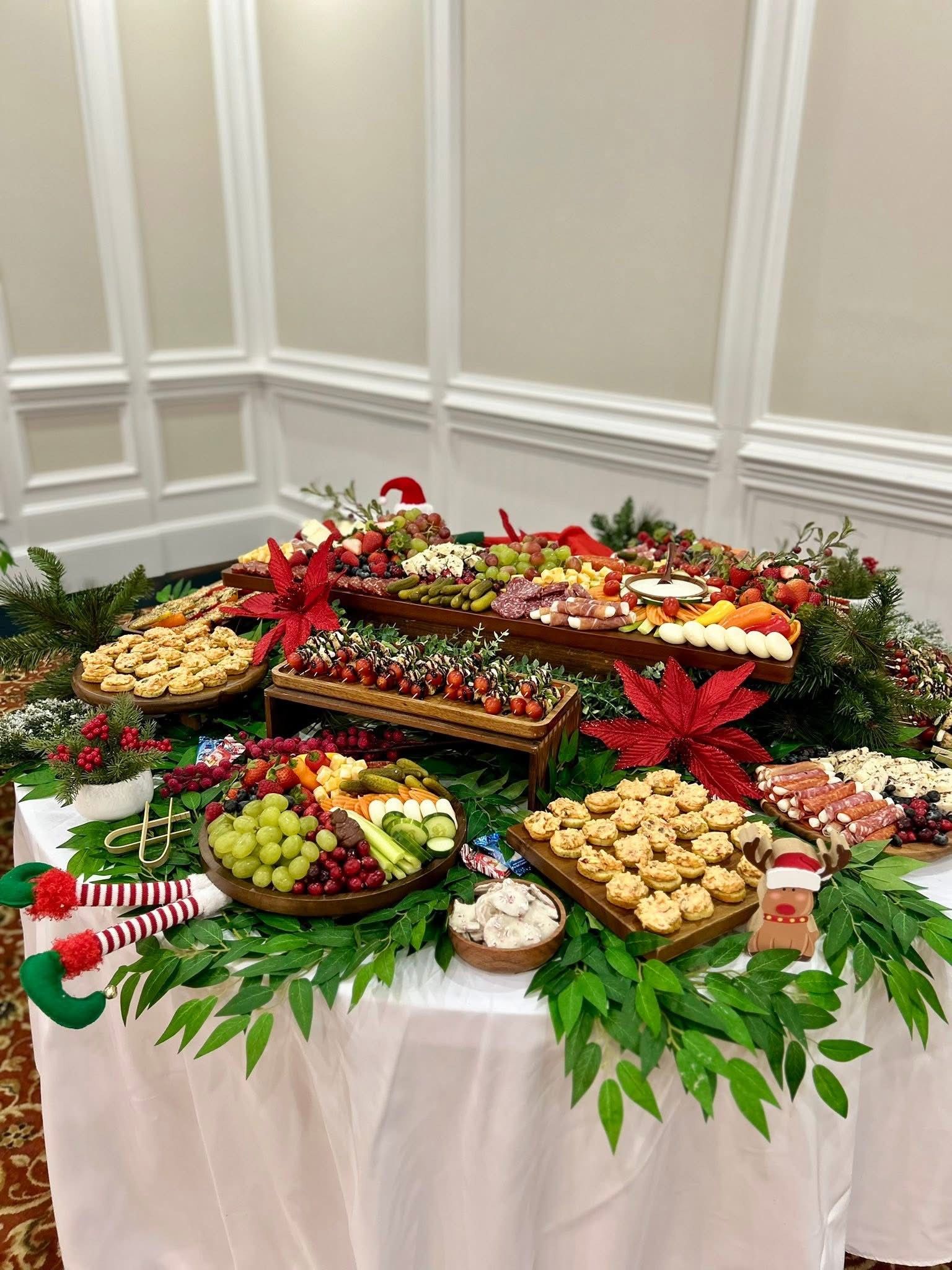 Festive food display on a table with fruit, crackers, and cheese, decorated with greenery and poinsettias.