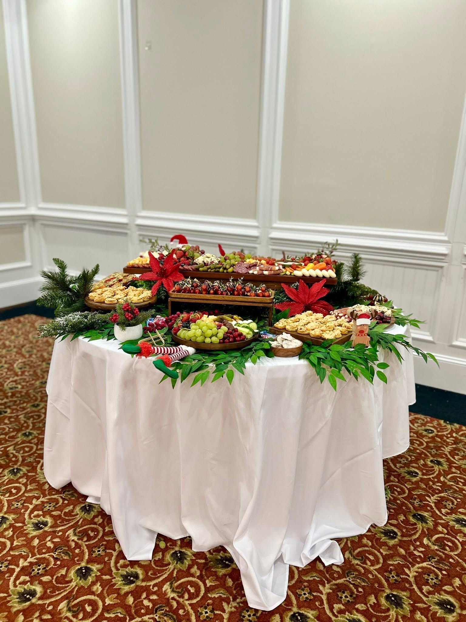 A buffet table with food platters, decorated for Christmas, on a round table with a white tablecloth.