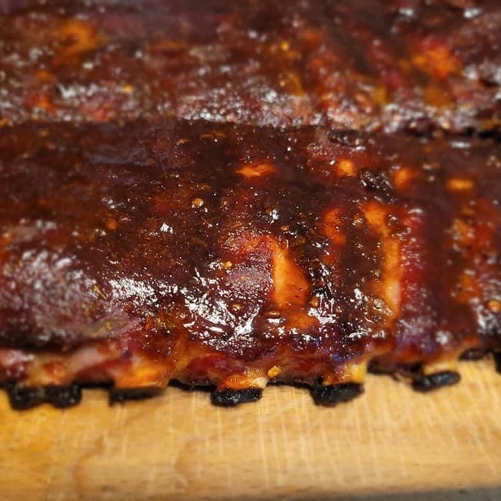 A close up of a piece of barbecue ribs on a wooden cutting board.