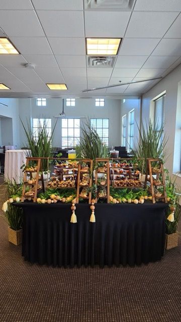 Buffet table with pastries, plants, and black tablecloth in a brightly lit room.