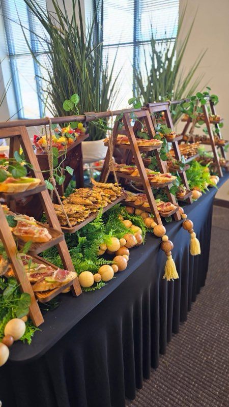 Buffet table with wooden ladders displaying food, decorated with greenery and beaded garland.