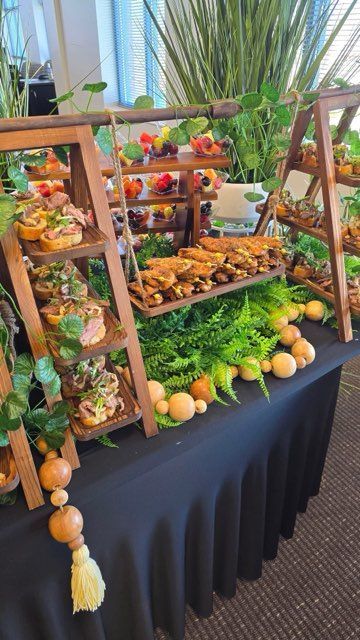 Catering table with food arranged on wooden ladder displays, with greenery and large decorative spheres.