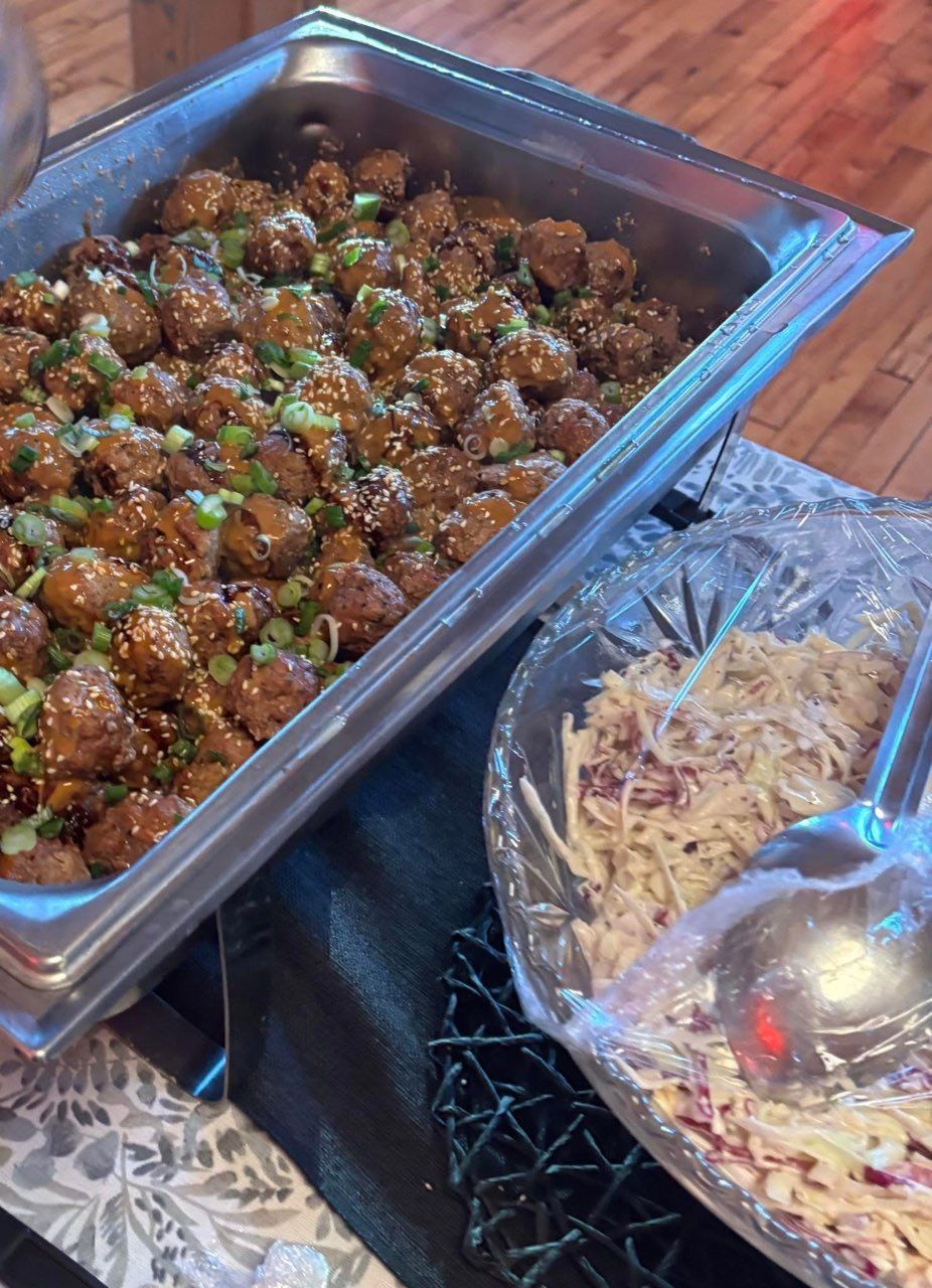 A buffet table with a tray of meatballs and a bowl of coleslaw.