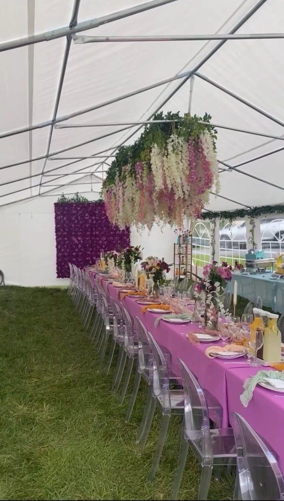 Long table set for an event under a tent, with overhead floral display and purple accents.