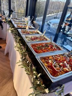 Buffet table with various food dishes, decorated with greenery, set indoors near a window overlooking a snowy scene.