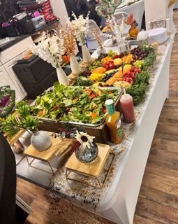 Buffet table with salad, fruit, and dressing, decorated with flowers.