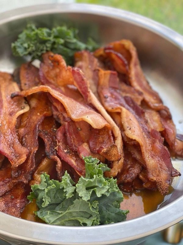 Pile of crispy bacon in a metal serving dish, garnished with green kale.