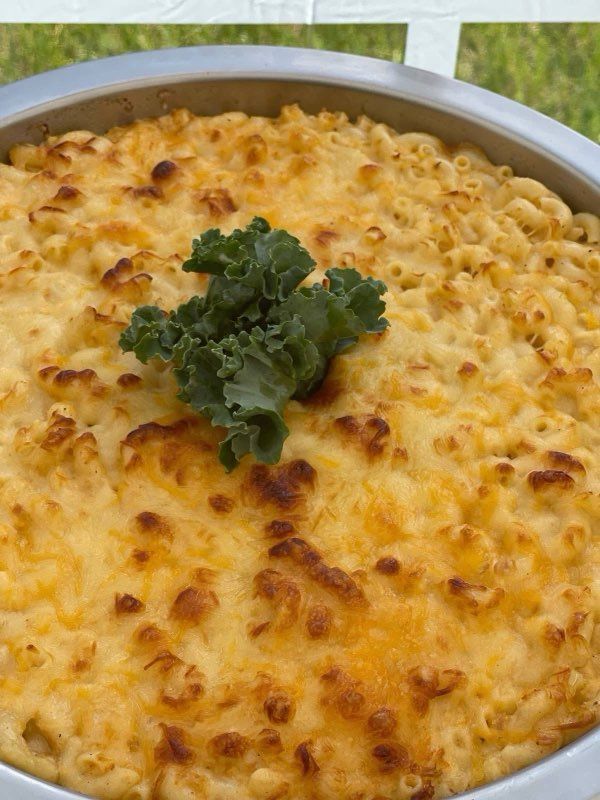 Baked macaroni and cheese in a metal pan, topped with a sprig of kale.
