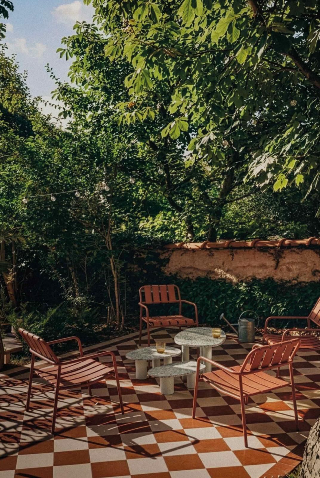 Twee stapels moderne, kleurrijke metalen stoelen staan tegenover elkaar op een houten terras in de buitenlucht, met een natuurlijke omgeving als achtergrond.