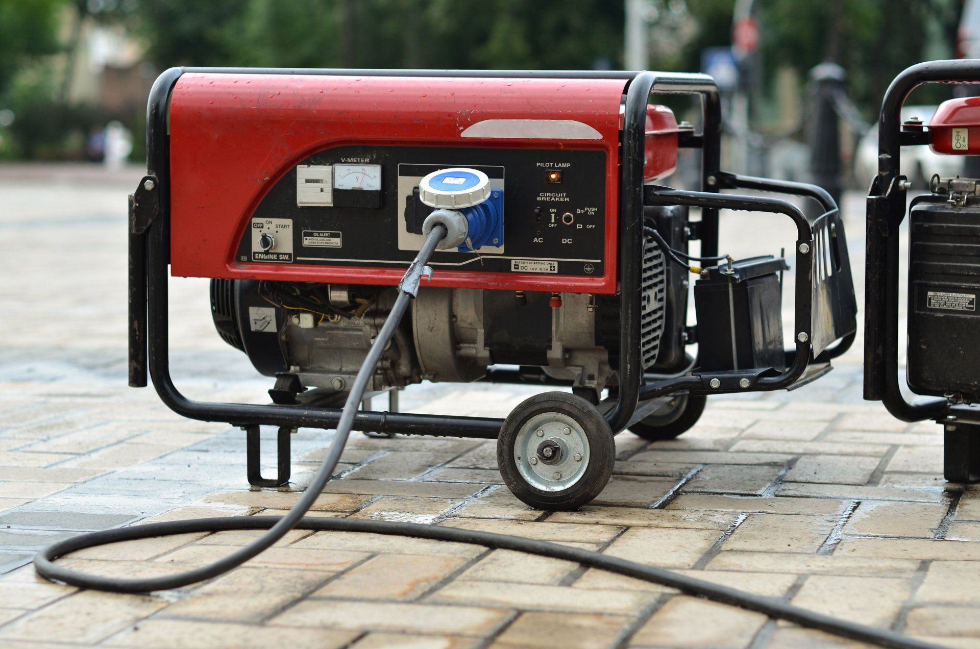 A red generator is plugged into a power cord on the sidewalk.
