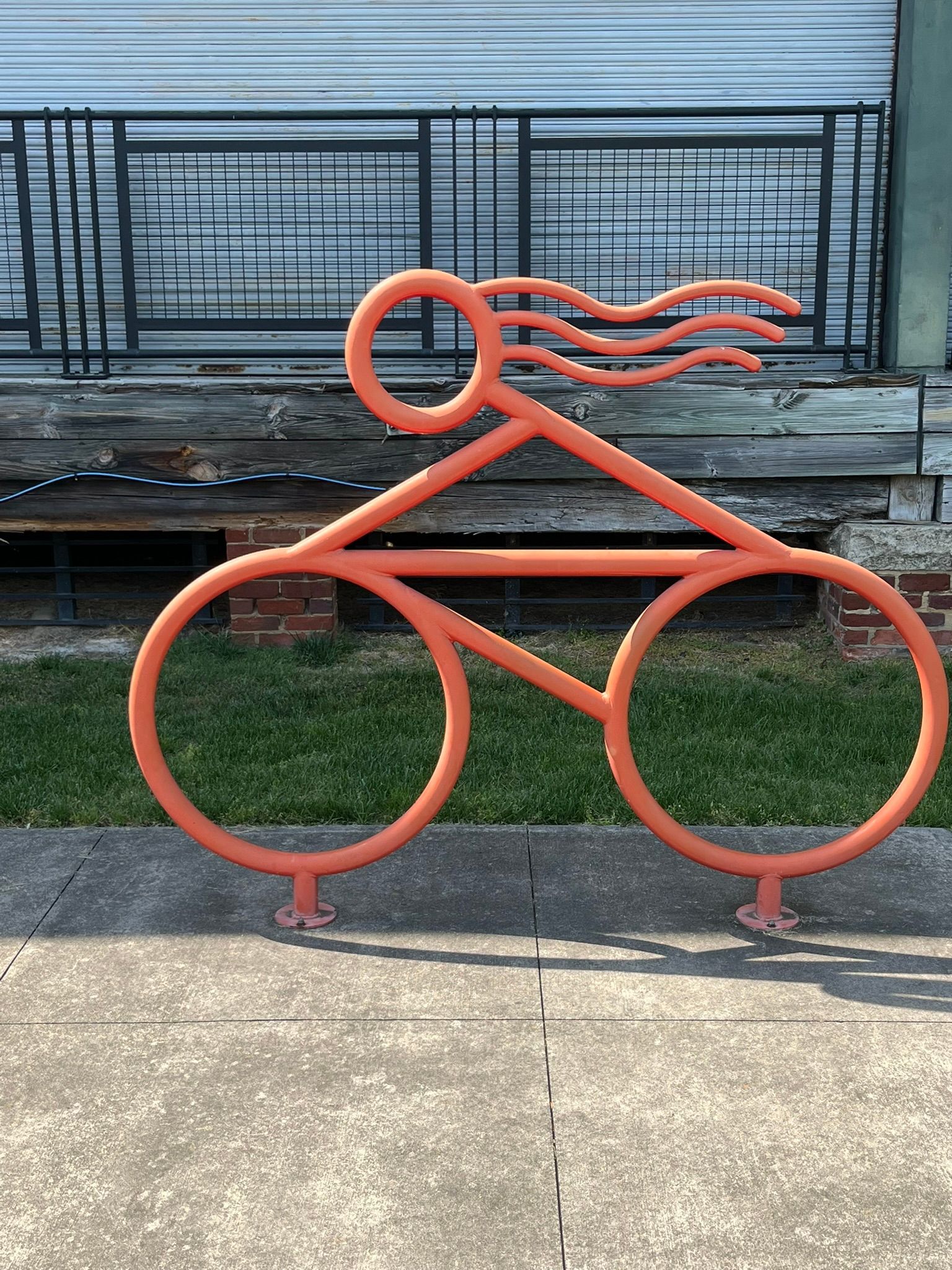 Orange metal bicycle sculpture with flowing hair on a sidewalk in front of a building.