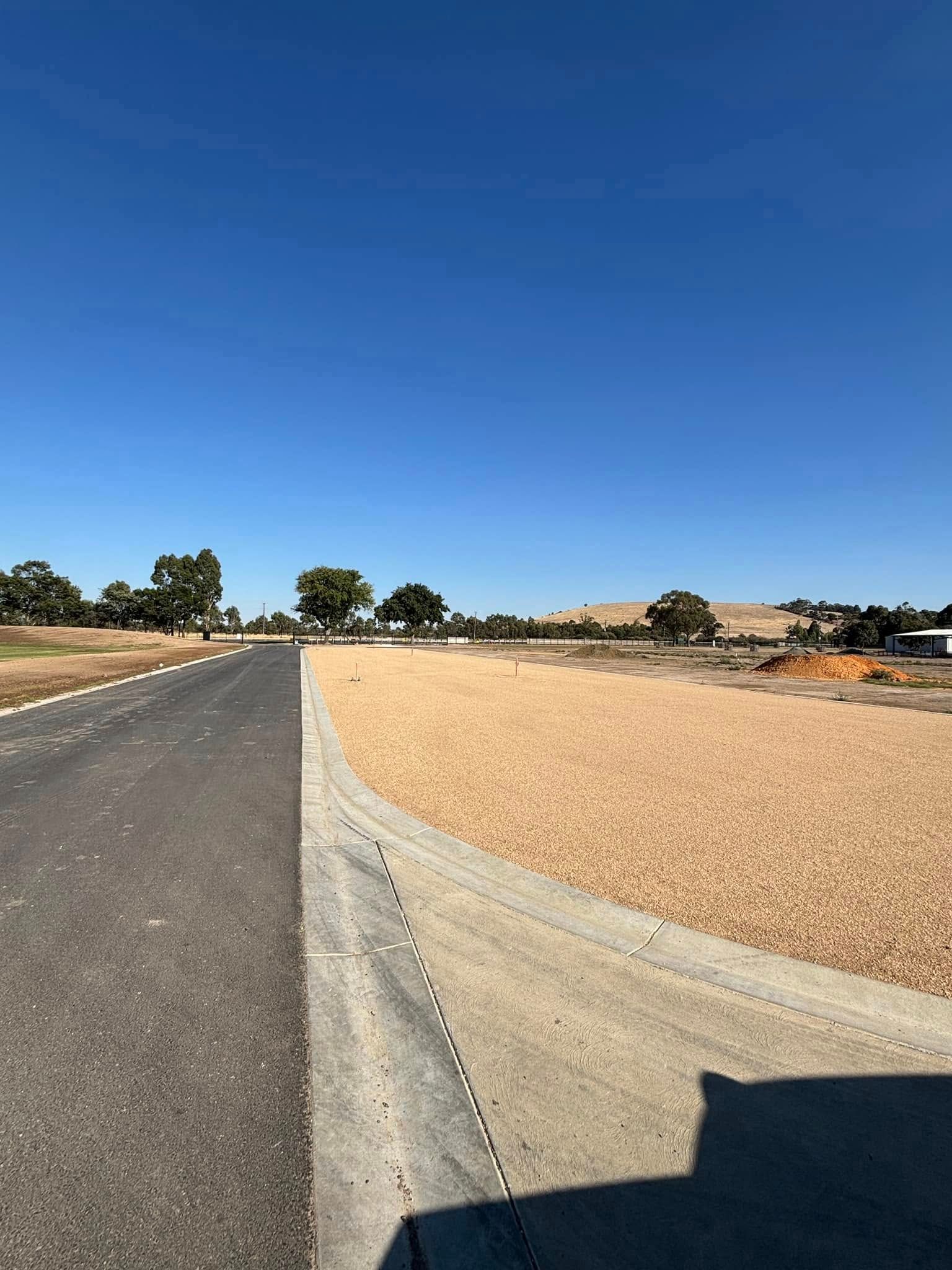 Empty paved road beside gravel turnout under a clear blue sky.