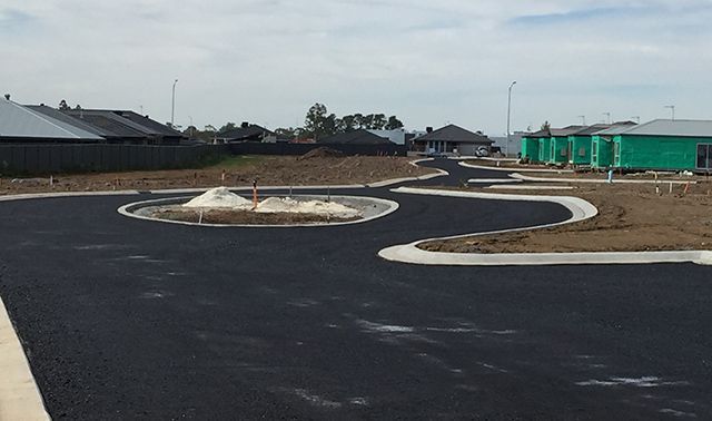 New asphalt road in a housing development with landscaped islands and houses in the background
