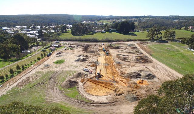 Aerial view of a large construction site with excavated earth and machinery beside green fields and trees