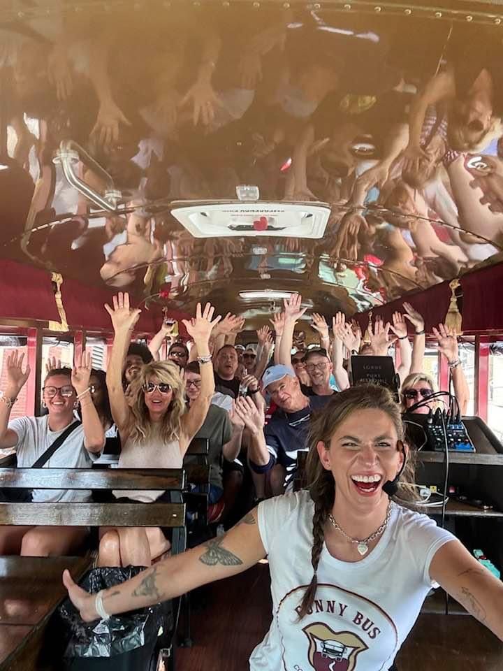 People cheering inside a colorful party bus, with hands raised and smiling faces.