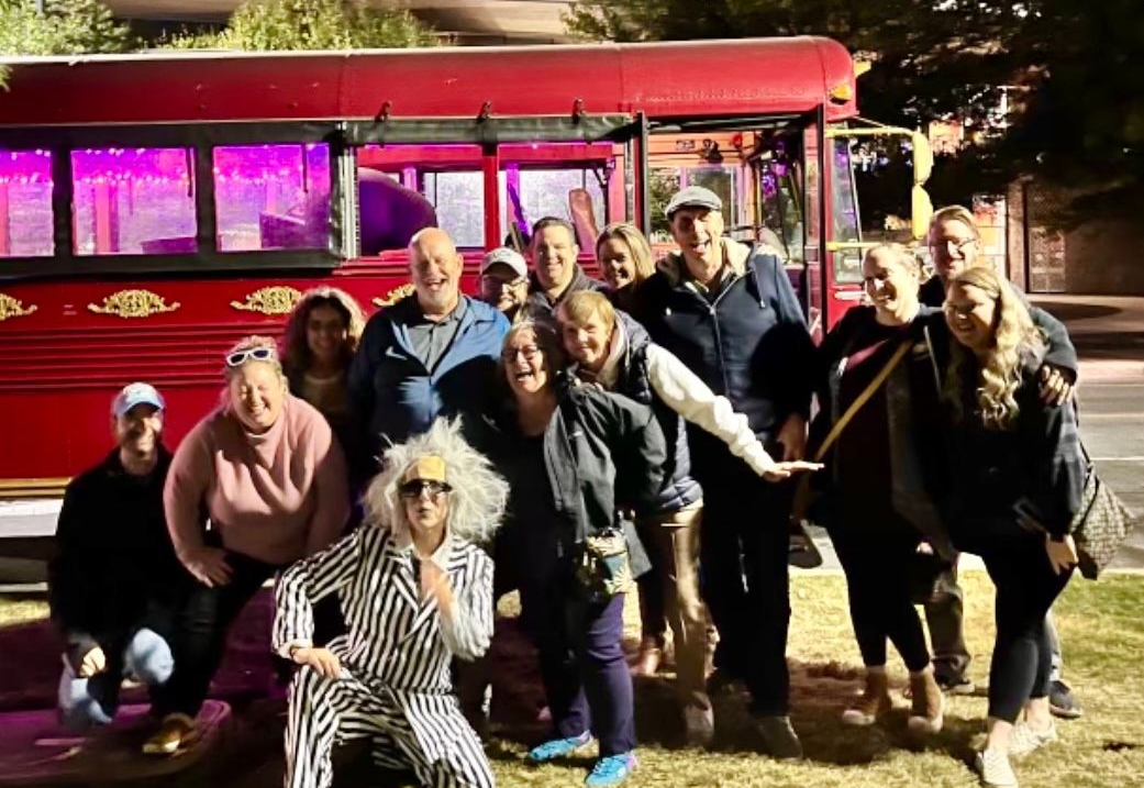 Group posing in front of a red bus at night, with purple-lit windows and a playful crouching person in front