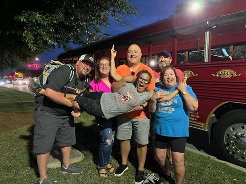Five friends posing and laughing beside a red trolley at night