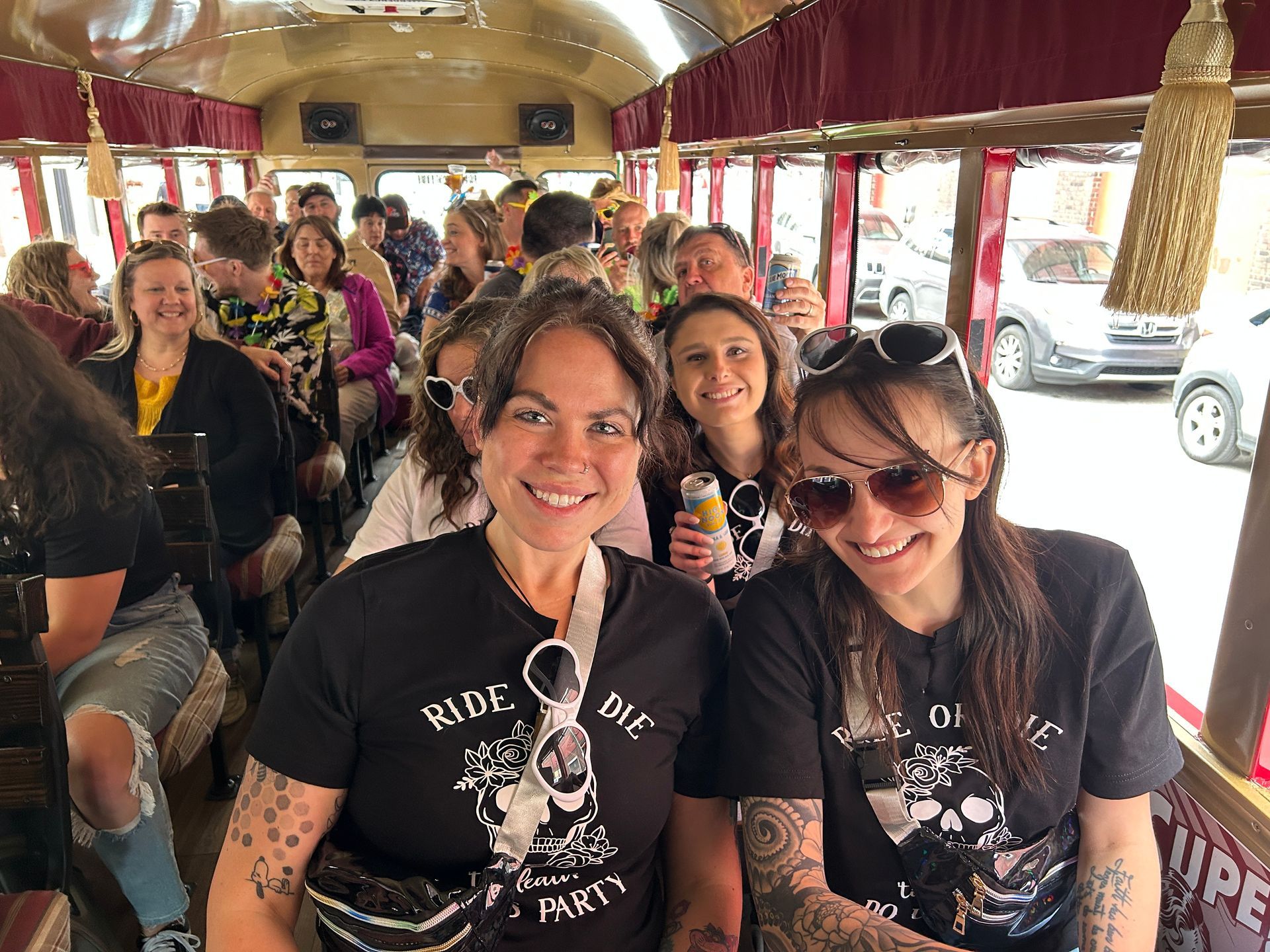 Two smiling women seated on a decorated trolley, with passengers and street views behind them.