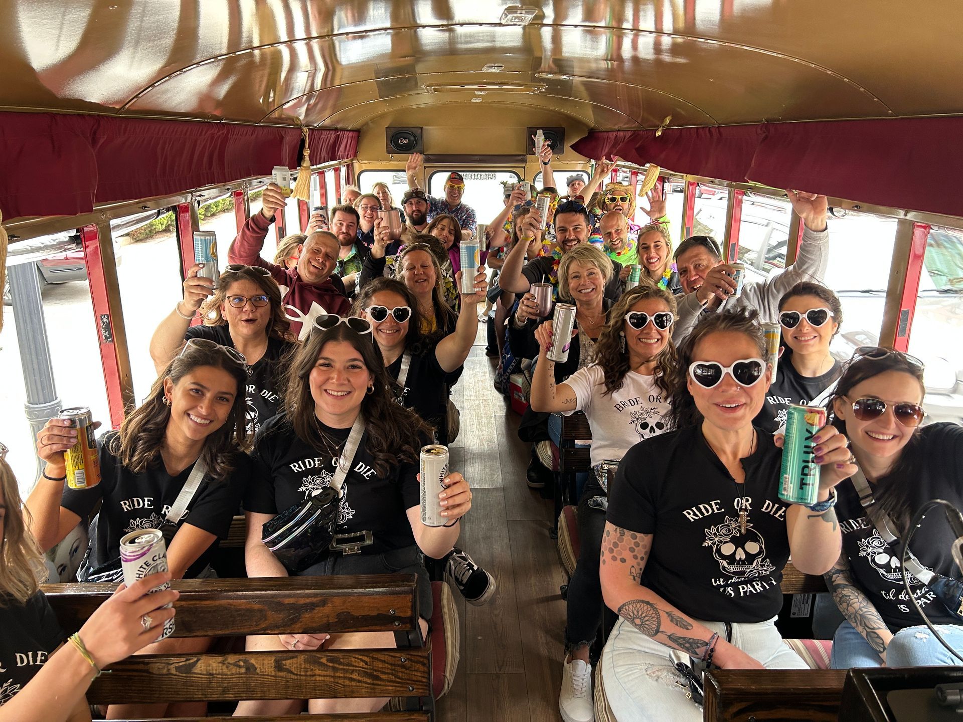 Group of people smiling and posing on a decorated party trolley with drinks inside a covered vehicle.