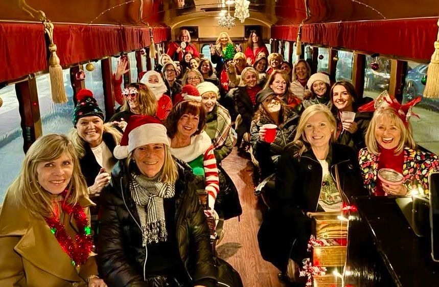 People in festive holiday attire smiling inside a decorated train carriage