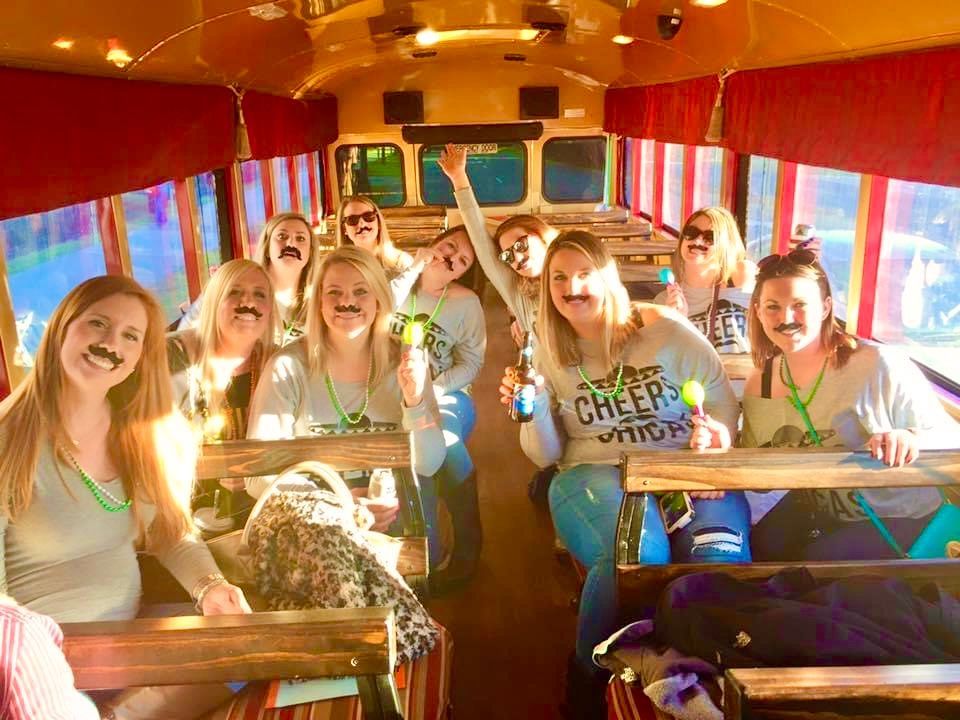 Group of smiling cheerleaders in a bus, wearing blue and white uniforms and holding pom-poms.