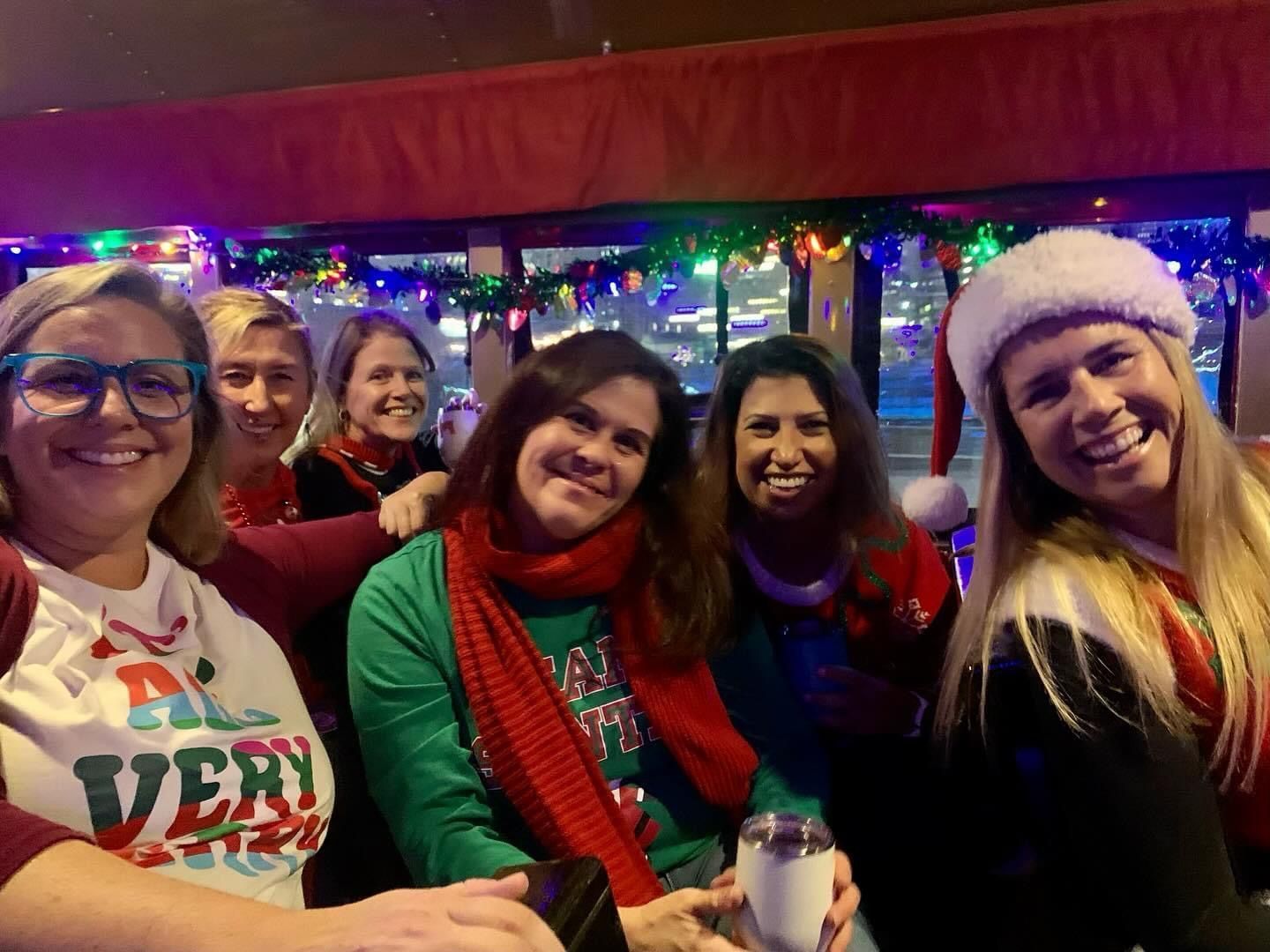 Friends smiling in festive sweaters and holiday hats at a colorful indoor party.