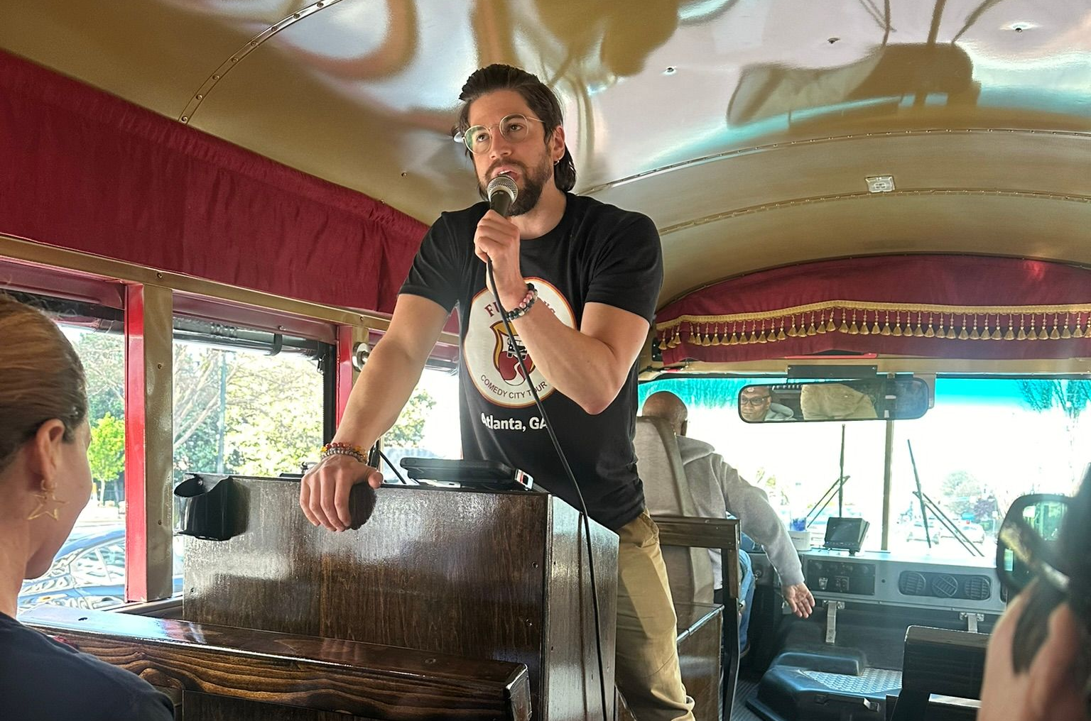 A comedian host with a microphone entertaining a busload of riders