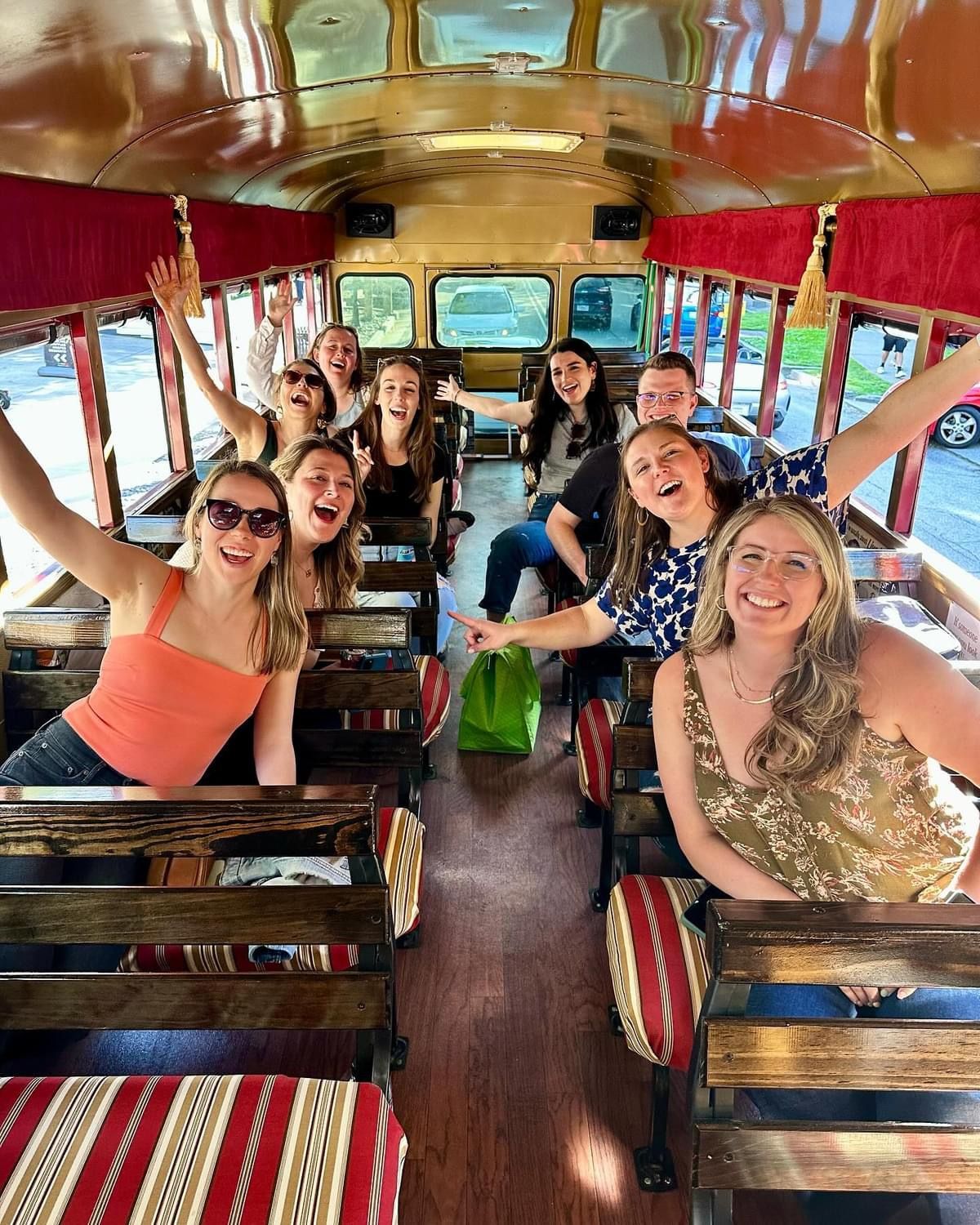 Group smiling on a colorful vintage bus with red curtains and wooden benches.