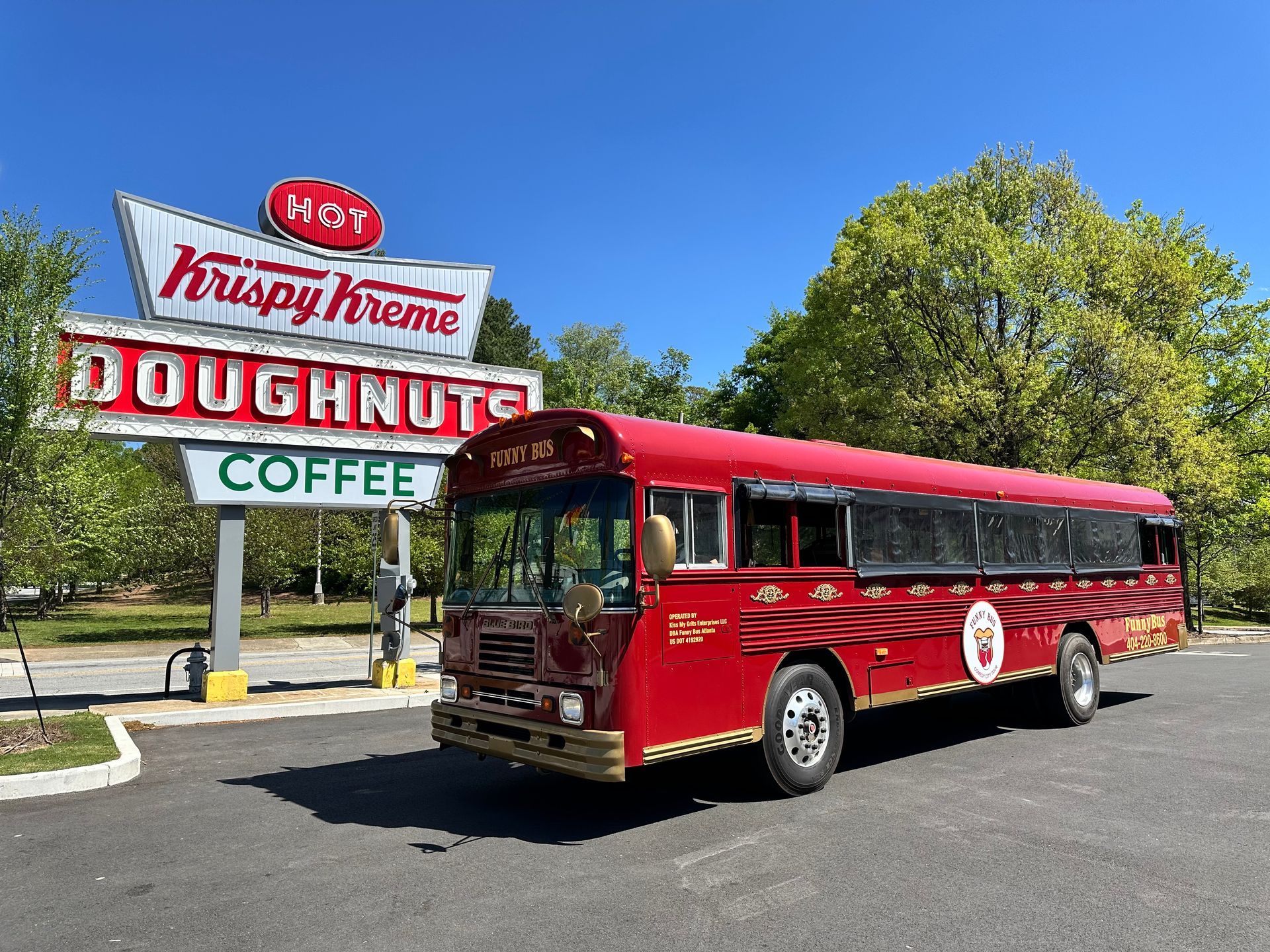Red Krispy Kreme bus parked beside a roadside Krispy Kreme Doughnuts sign on a sunny day