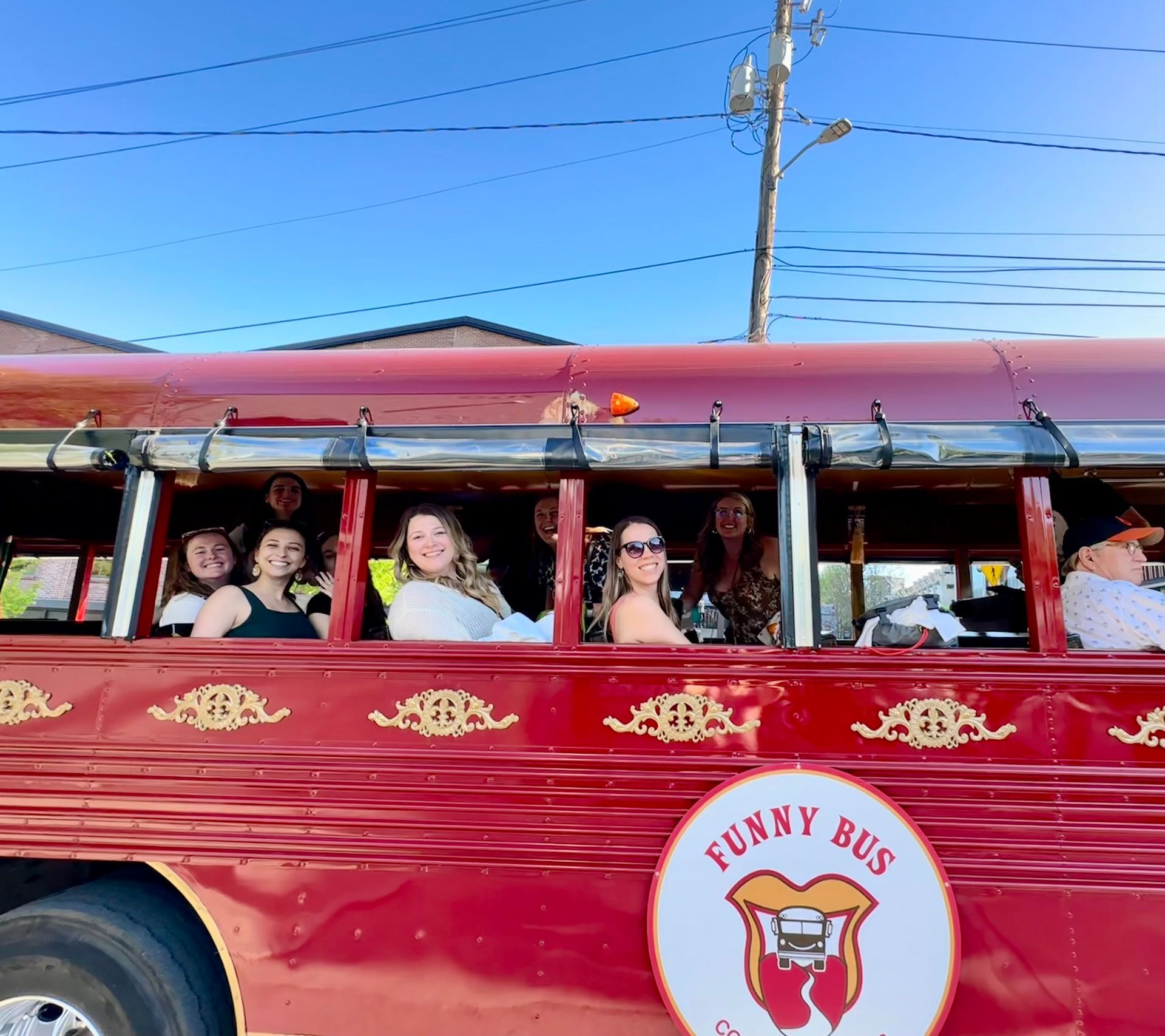 Red open-air bus with passengers waving under a clear blue sky, labeled “Funky Bus” on the side.