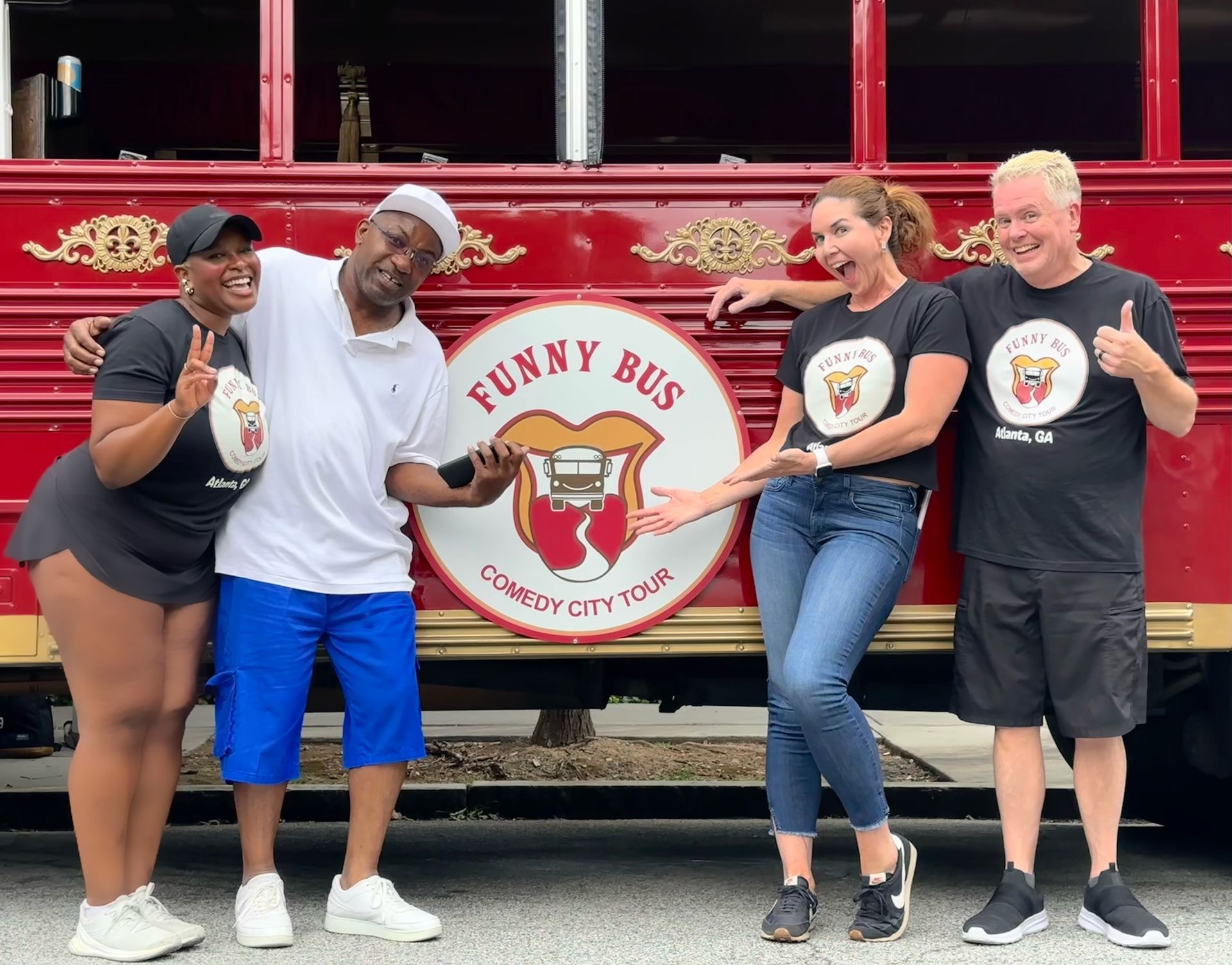 Four people stand in front of a red bus with
