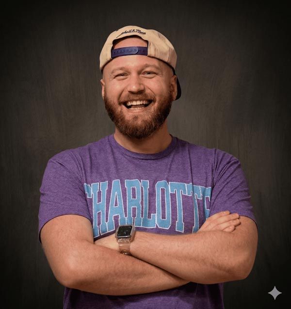 Man with a red beard smiles, yellow parakeet on his shoulder, gray shirt, dark suspenders.
