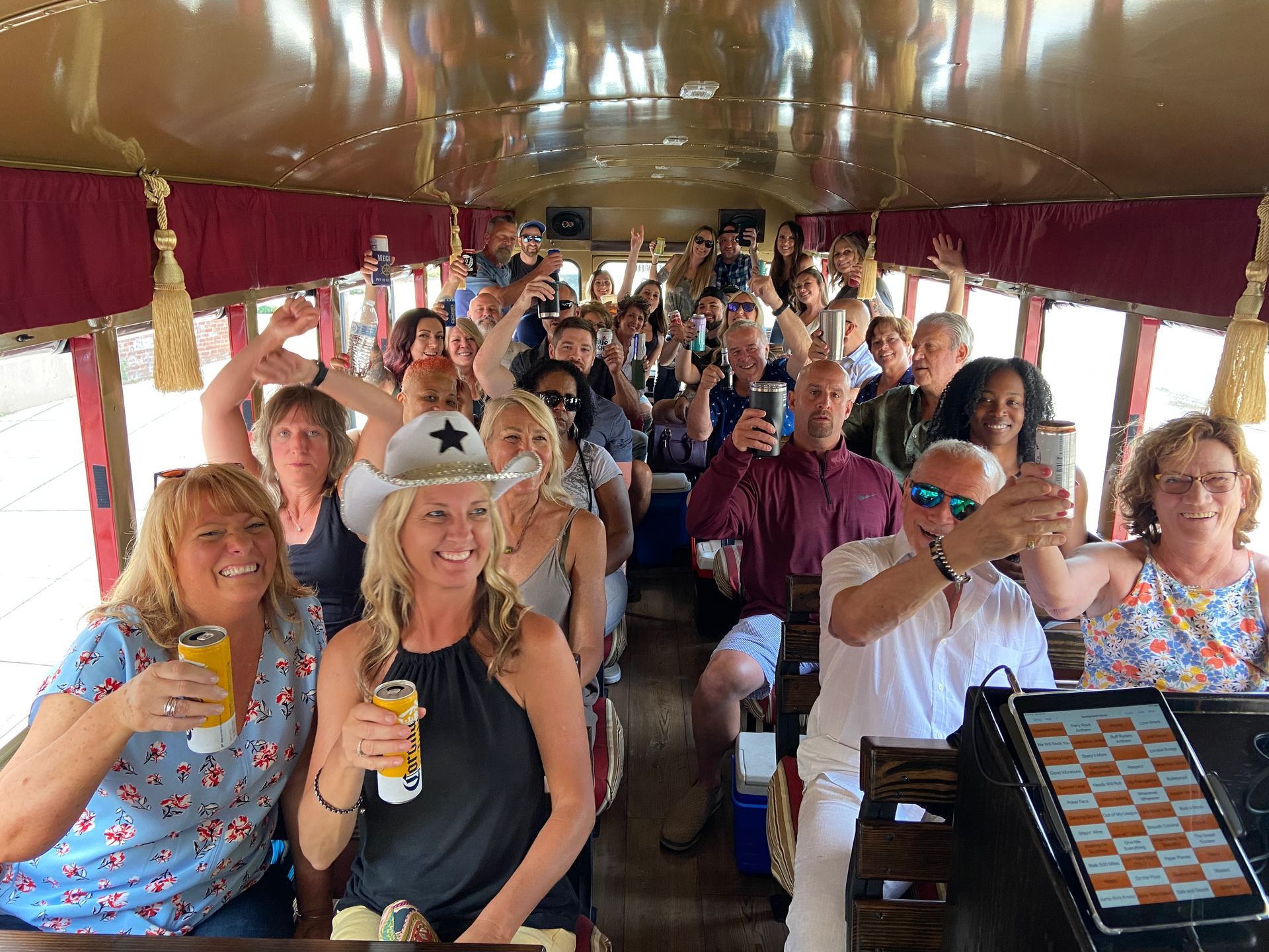 Passengers on a party bus raise drinks and smile inside a red-draped vehicle.